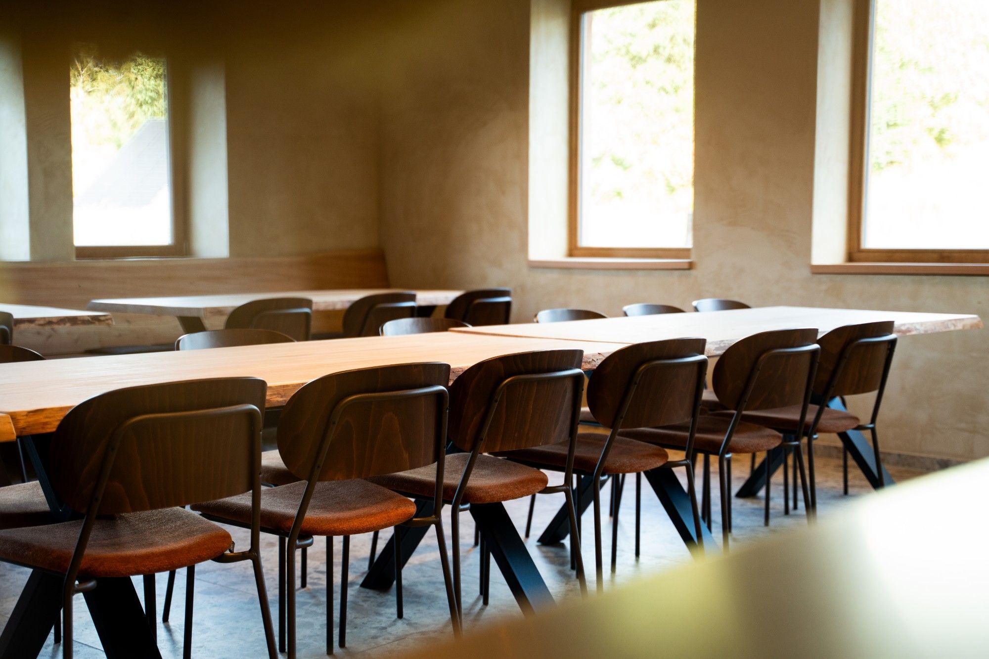 La salle commune avec de longues tables en bois massif et des chaises en cuir cognac